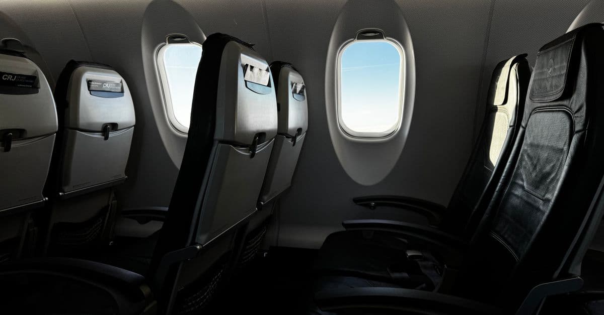 Rows of empty economy seats in an airplane cabin, looking down the aisle.